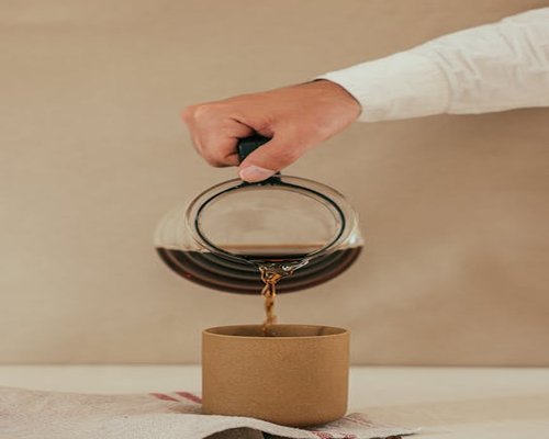 A hand pouring coffee slowly into a ceramic mug